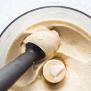 A blender filled with creamy banana nice cream, with a black tamper blending the mixture.