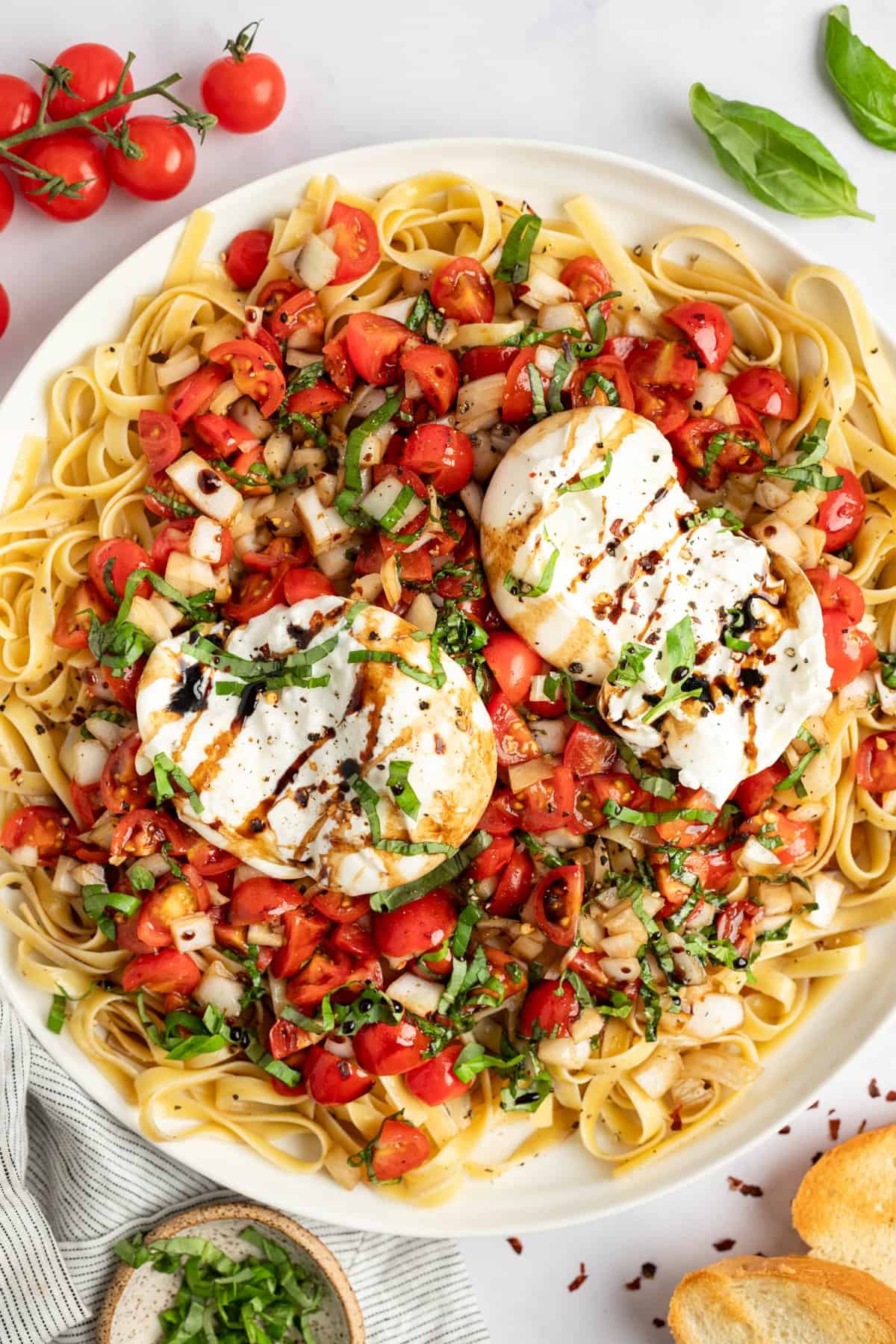 A plate of pasta topped with fresh chopped tomatoes, basil, two poached eggs, and a drizzle of balsamic glaze, garnished with black pepper.