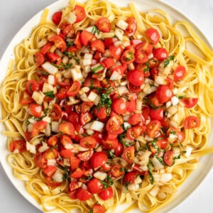 A plate of fettuccine pasta topped with chopped tomatoes, onions, and herbs.