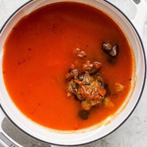 A pot containing tomato soup with herbs and vegetables visible on the surface.