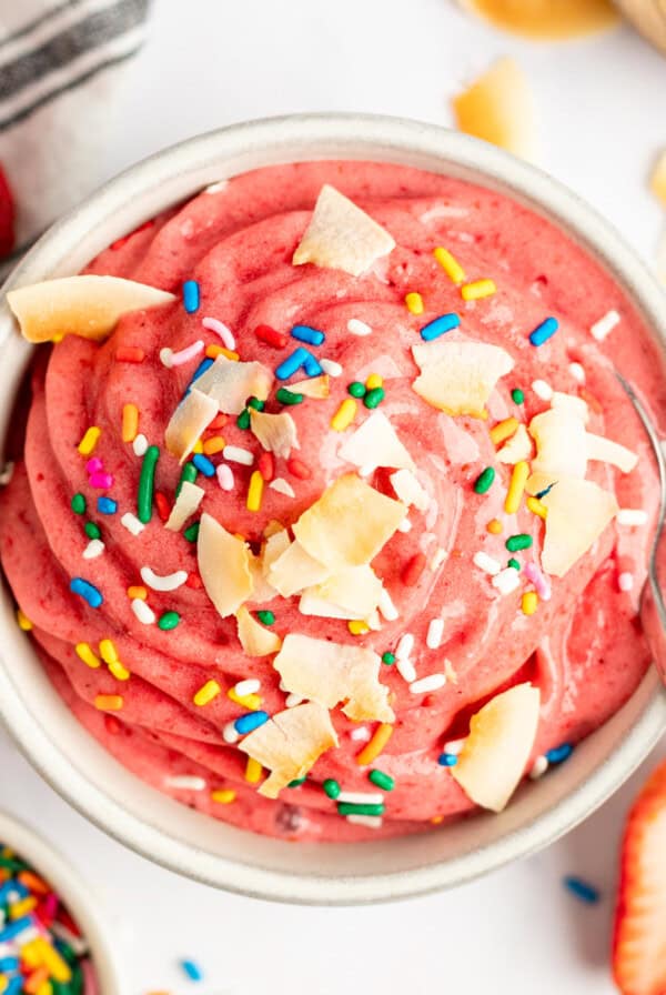 A vibrant pink smoothie bowl topped with coconut flakes and colorful sprinkles, viewed from above.