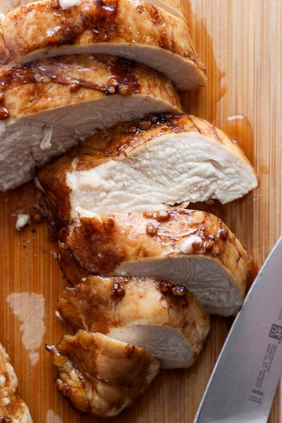 Sliced grilled chicken breast with crispy skin on a wooden cutting board, next to a chef's knife.