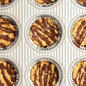 A baking sheet with nine muffin tin liners filled with a mixture topped with drizzled chocolate.