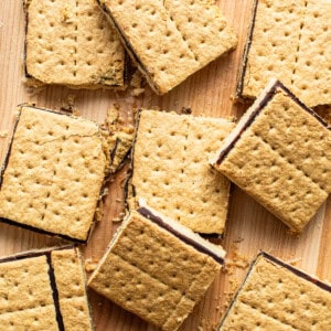 Smores bars with a gooey chocolate filling, scattered on a wooden surface.