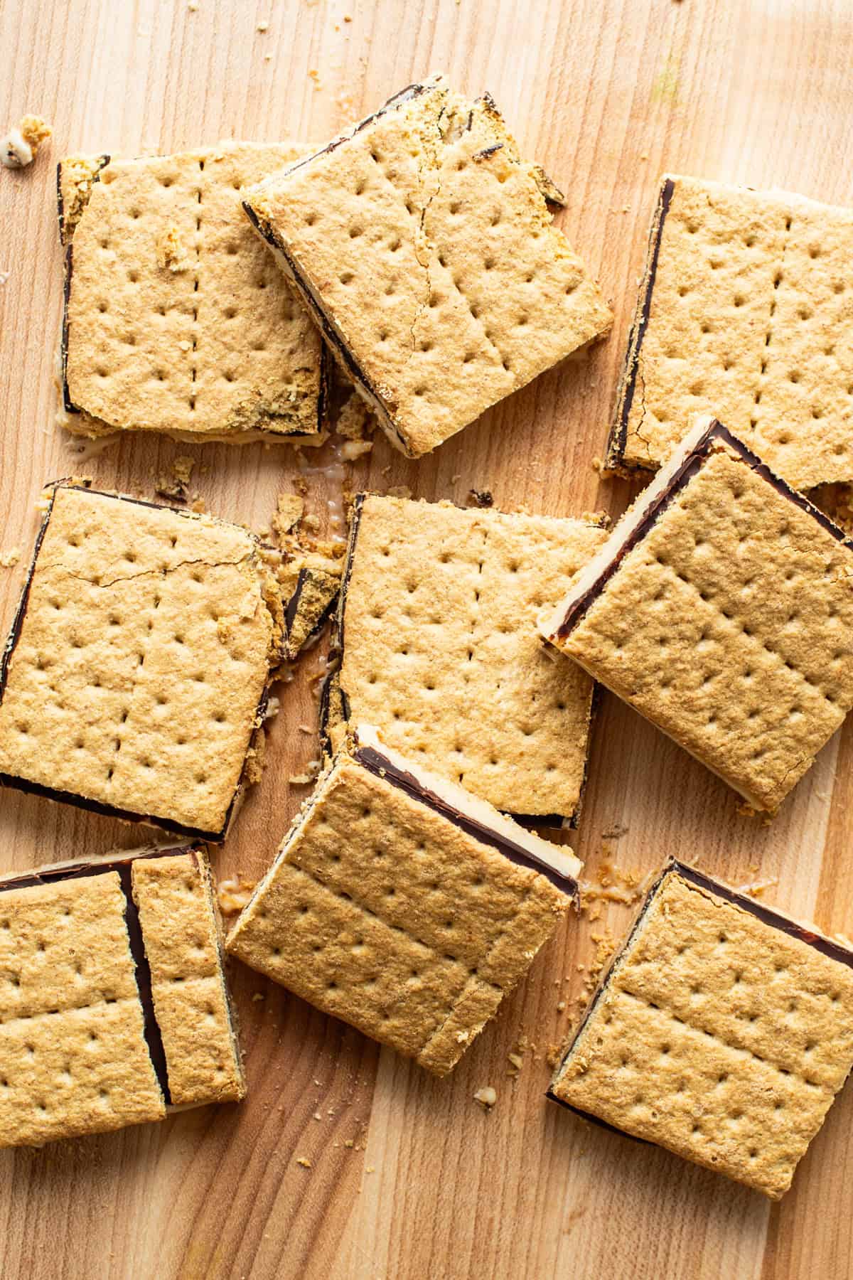 Smores bars with a gooey chocolate filling, scattered on a wooden surface.