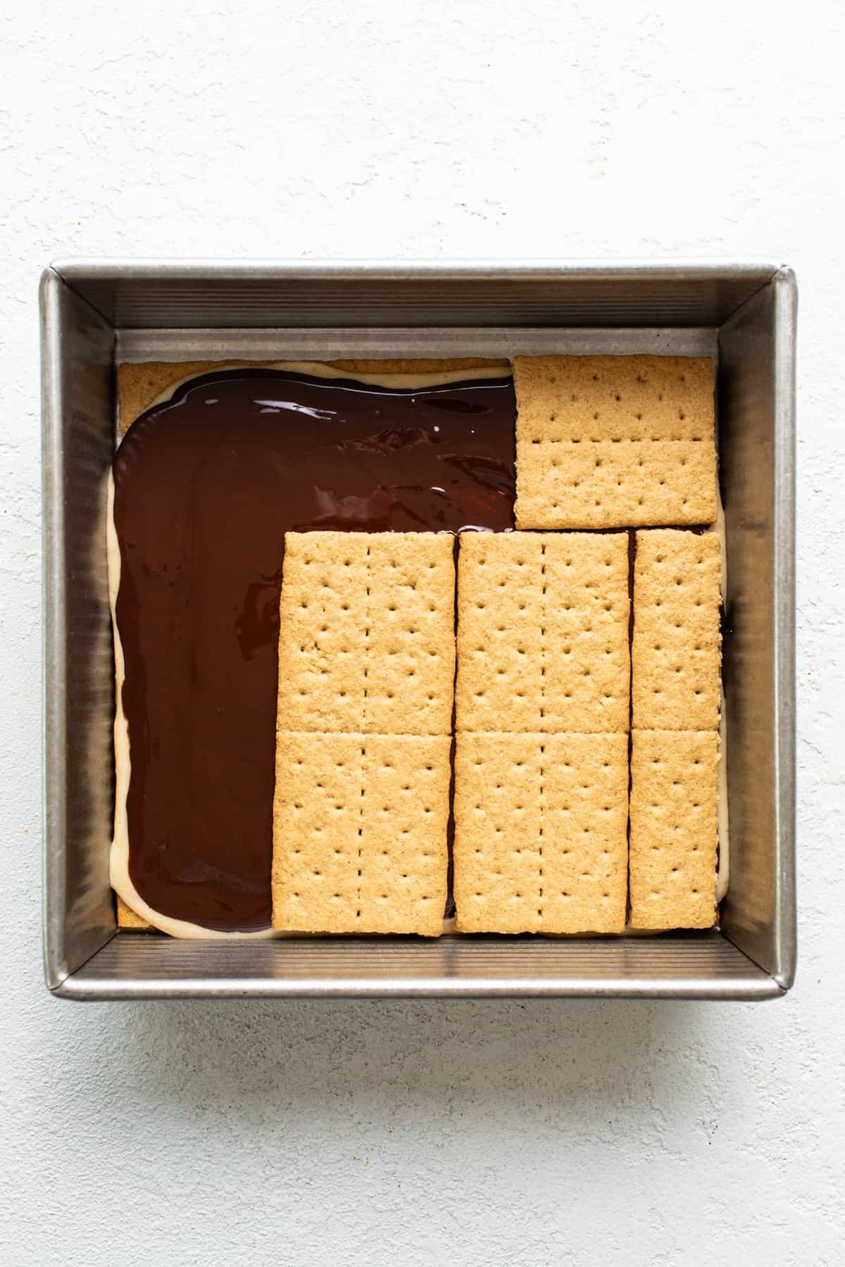 A baking dish with a layer of chocolate topped by aligned graham crackers, preparing for a s'mores dessert.