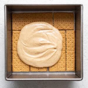 A square baking dish filled with graham crackers topped with a layer of smooth, creamy filling.