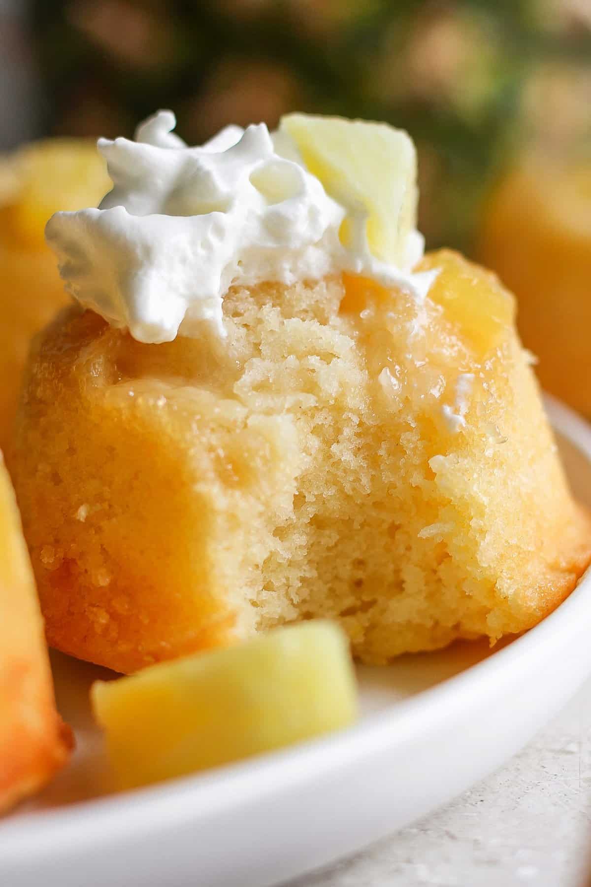 Close-up of a pineapple upside-down cake with a dollop of whipped cream on top, served on a white plate.