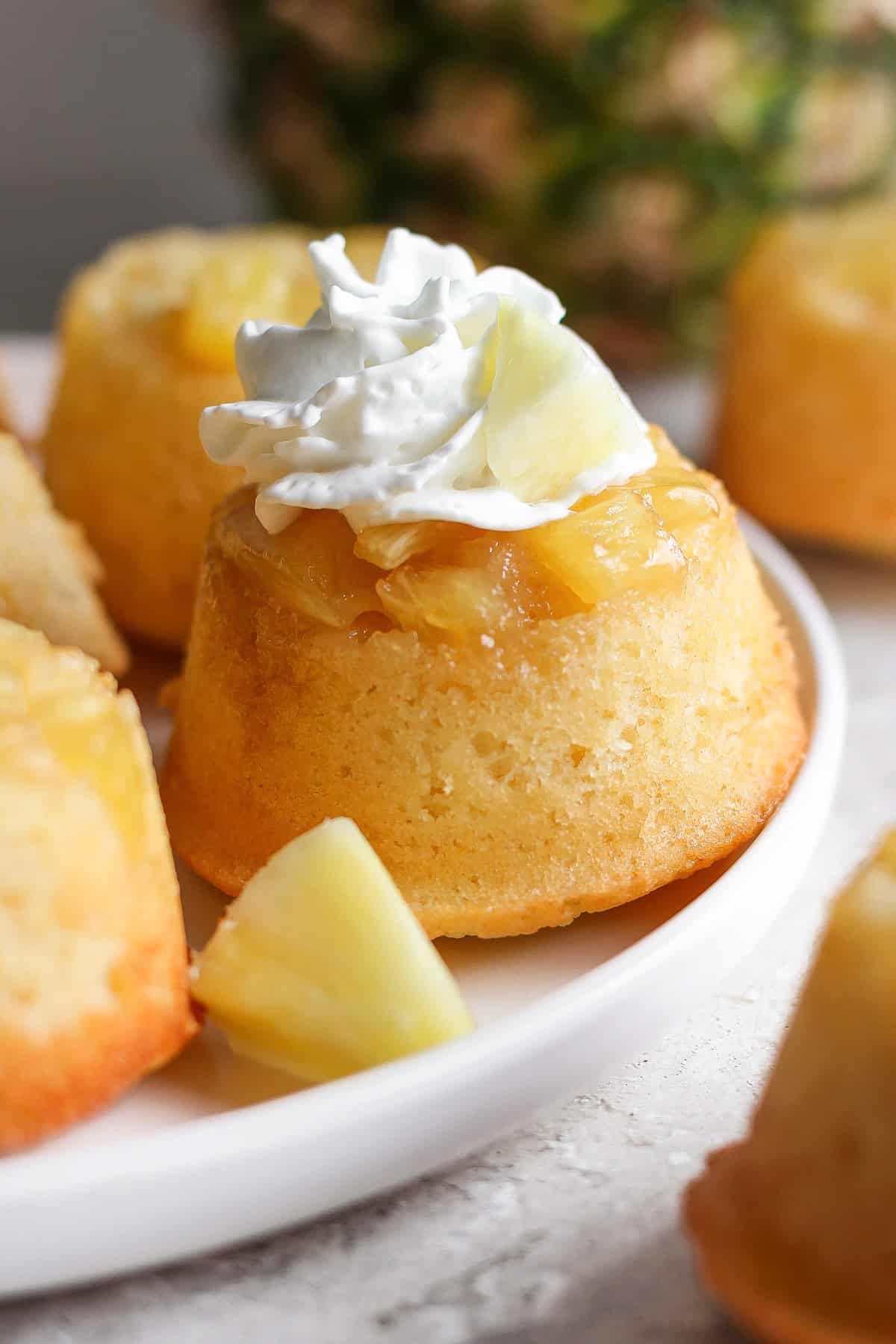 Individual pineapple upside-down cakes topped with whipped cream and pineapple chunks on a white plate.