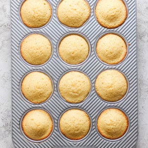 Freshly baked muffins in a 12-cup muffin tray with a striped pattern, viewed from above on a light surface.