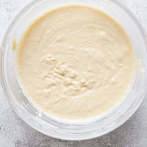 Top view of a glass bowl containing freshly prepared, smooth bread dough on a white surface.