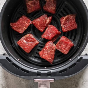 Raw beef pieces arranged in an air fryer basket, ready for cooking.