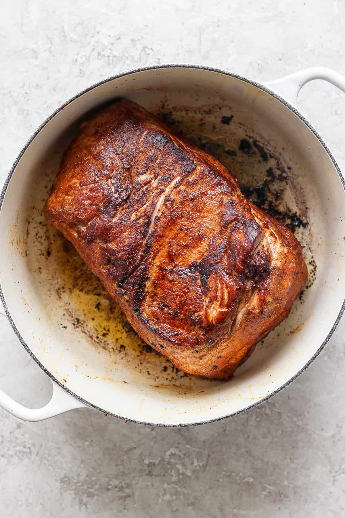 A cooked, browned piece of meat in a white pot, showing seared and crispy edges.