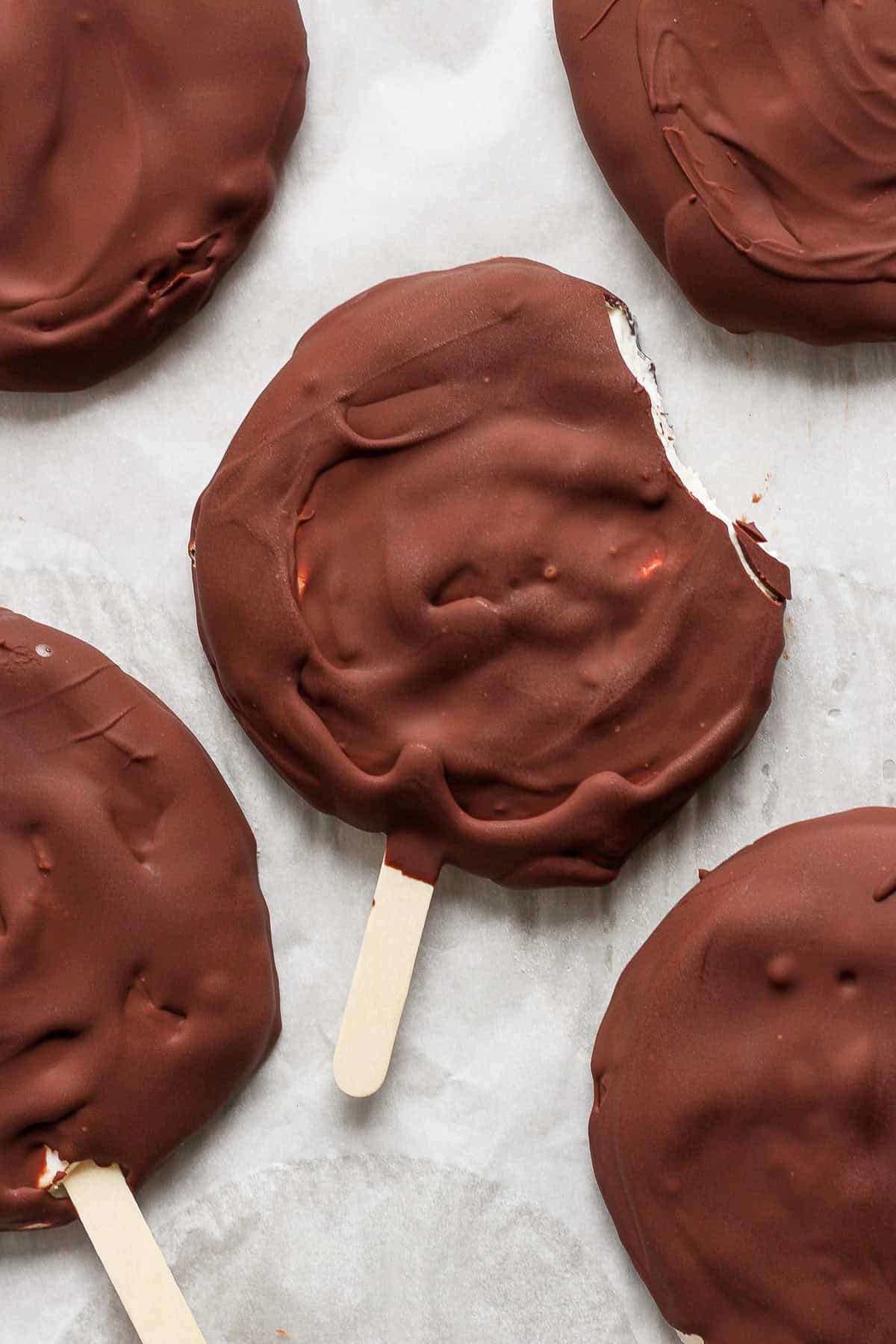 Chocolate-covered ice cream bars on sticks, viewed from above, with one bar having a bite taken out of it.