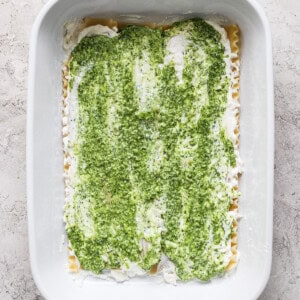 A white baking dish containing an uncooked layered green and white lasagna against a textured light gray surface.