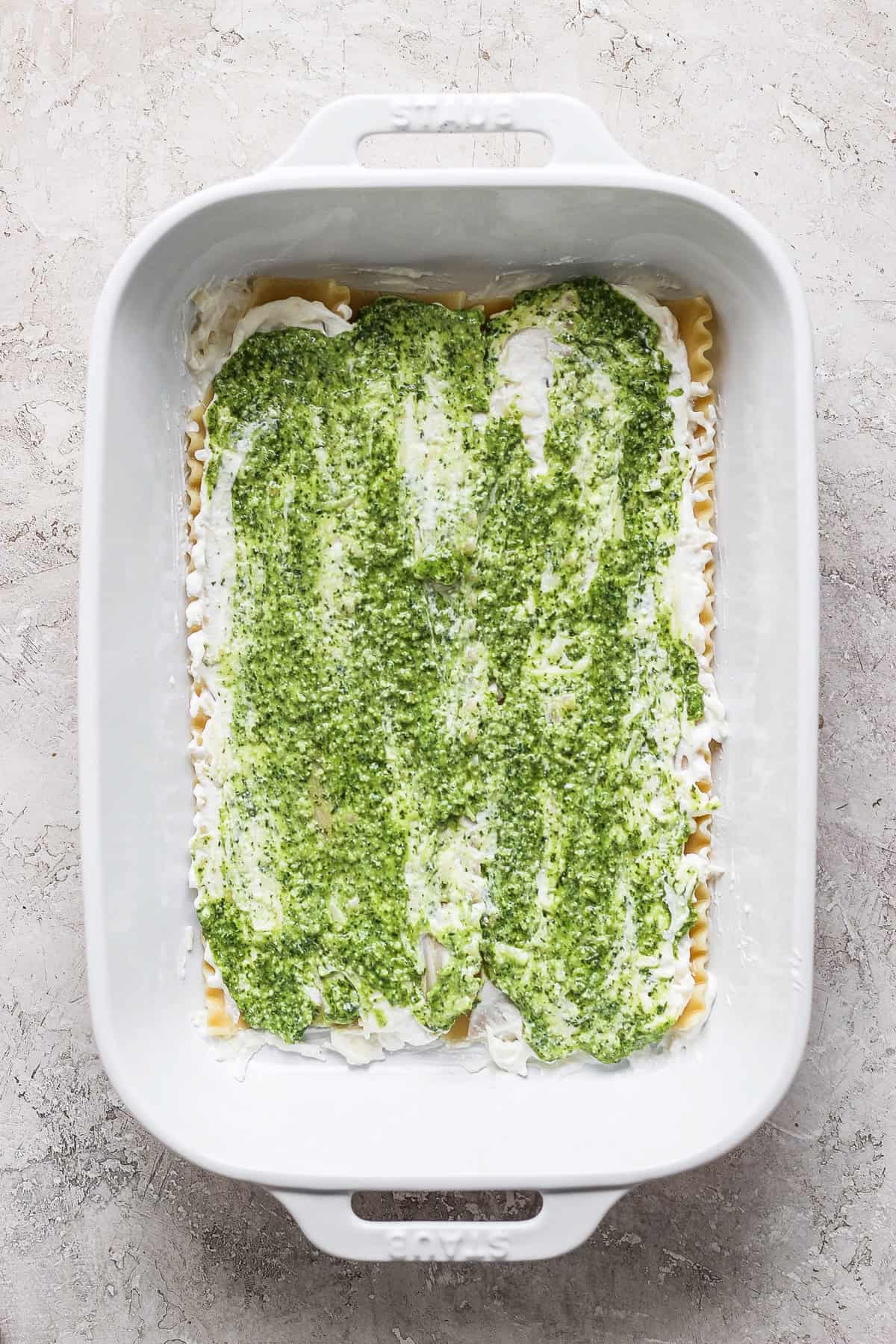 A white baking dish containing an uncooked layered green and white lasagna against a textured light gray surface.