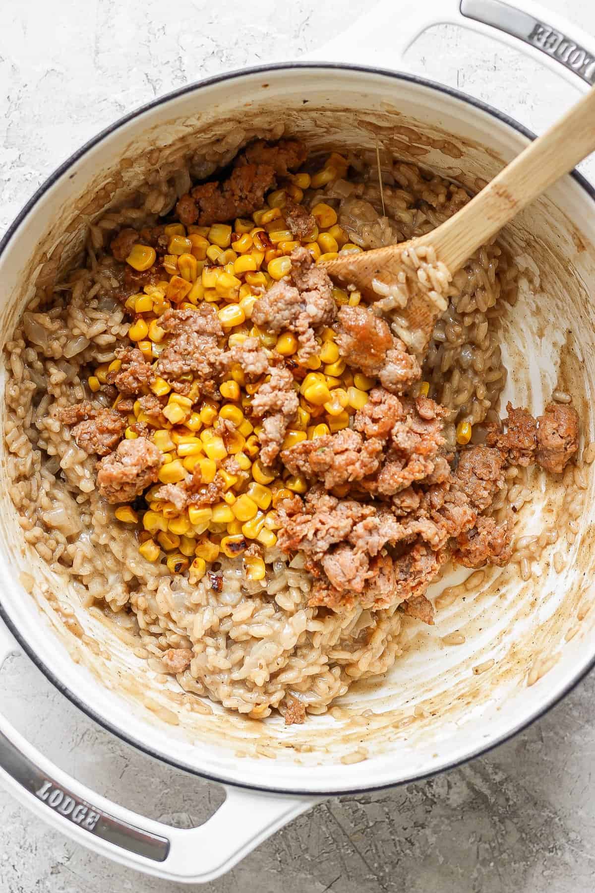 A pot of risotto with corn and ground sausage being stirred with a wooden spoon.