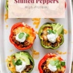 A white dish with red and green bell peppers stuffed with a mix of ingredients, topped with melted cheese, avocado slices, cilantro, and a dollop of sour cream. Text overlay reads "Easy Stuffed Peppers High-Protein!.