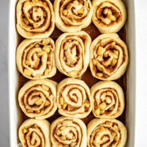 A baking dish that contains twelve unbaked cinnamon rolls arranged in rows on a light-colored surface.