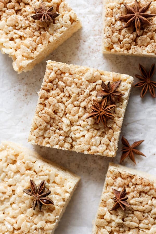 Square rice crispy treats with a dusting of spices and garnished with star anise, arranged on a parchment paper surface.