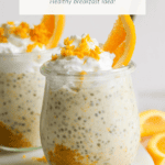 Two jars of Creamsicle Overnight Oats topped with whipped cream, orange zest, and orange slices, are displayed on a white surface with additional orange slices nearby.