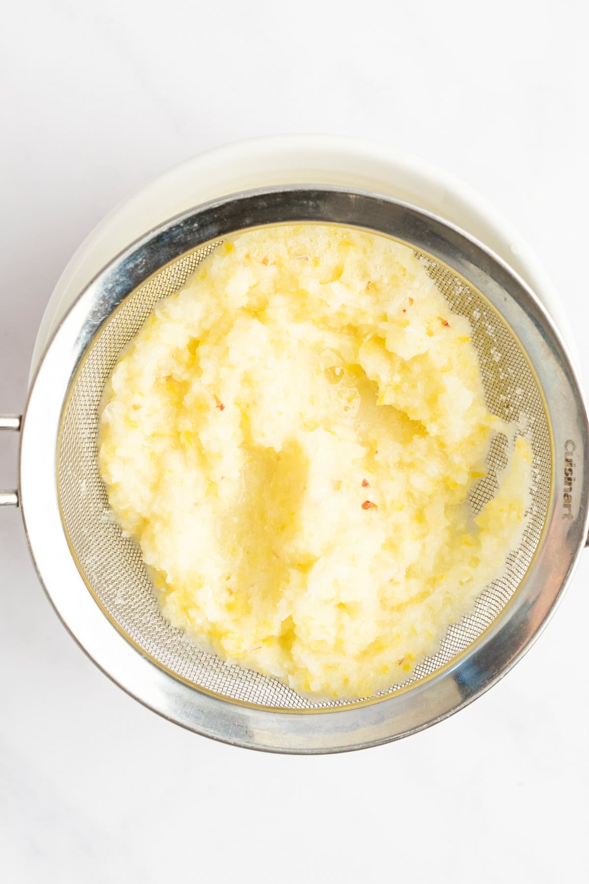 A metal sieve containing mashed potatoes over a white bowl.