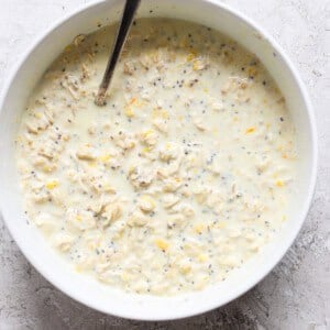 A bowl of oat mixture with chia seeds and grated lemon zest, reminiscent of creamsicle overnight oats, stirred with a spoon.