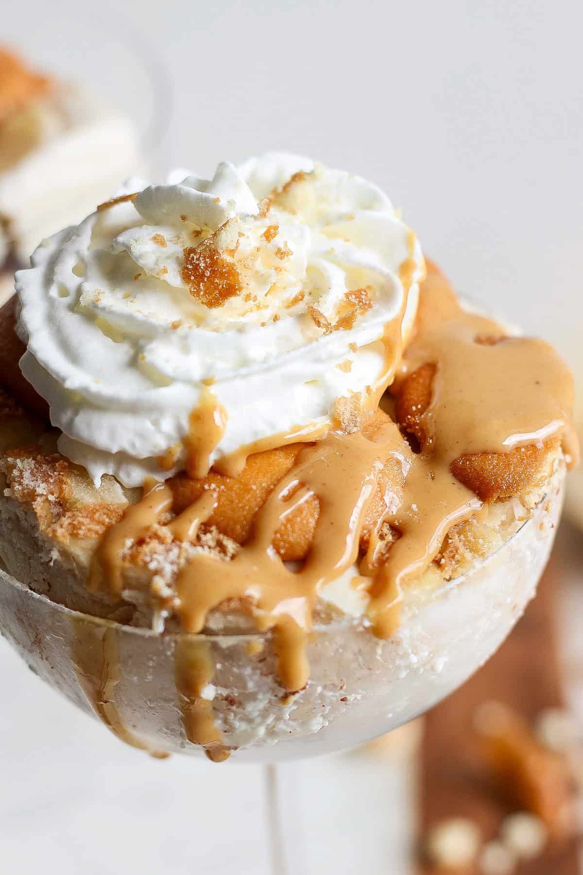 Close-up of a peanut butter banana ice box cake topped with whipped cream, caramel sauce, and cookie crumbs, served in a glass container.