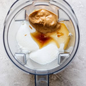 A blender containing yogurt, peanut butter, vanilla extract, and honey viewed from above evokes the creamy richness of a peanut butter banana ice box cake.