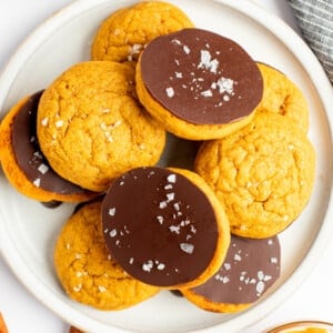 A plate of cookies, with some topped with a layer of chocolate and sea salt flakes, arranged on a white plate.