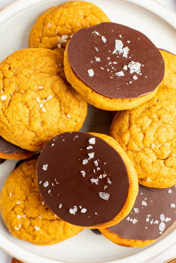 A plate of cookies, with some topped with a layer of chocolate and sea salt flakes, arranged on a white plate.