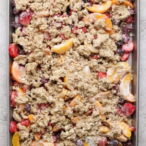 A baking tray filled with a mixture of sliced fruits, including peaches and berries, topped with a crumbly oat mixture, ready to be baked.