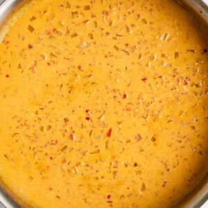 A metal pan filled with a thick, orange-colored soup or sauce that contains small pieces of diced vegetables.