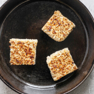 Three toasted Rice Krispie treats in a cast iron skillet on a light textured surface.