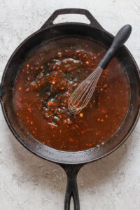 A black cast iron skillet filled with a dark brown sauce and a whisk resting inside.