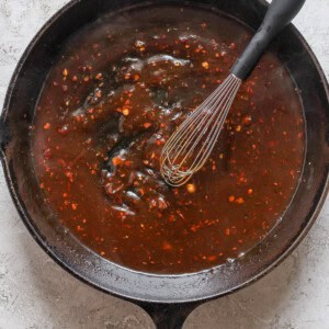 A black cast iron skillet filled with a dark brown sauce and a whisk resting inside.