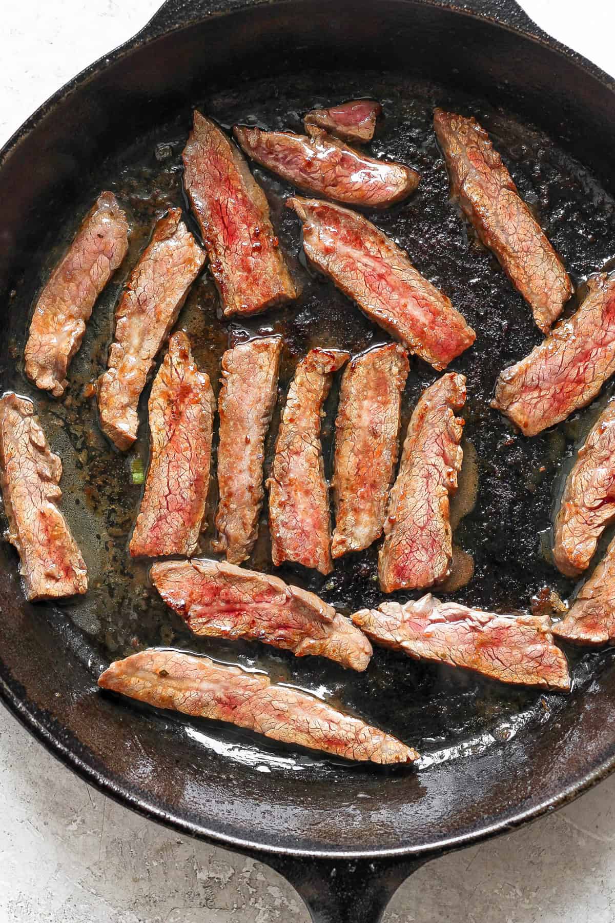 Slices of cooked meat in a black skillet.