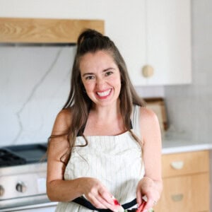 A fit foodie finds joy in her modern kitchen, smiling while preparing a delicious meal. She is wearing an apron.