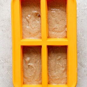 A yellow four-section silicone mold is filled with light brown batter on a light gray textured surface.