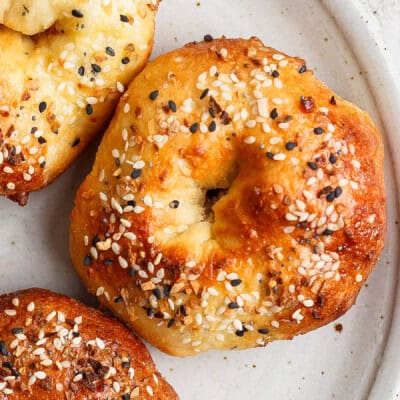 Close-up of three bagels topped with sesame seeds and other seasonings on a beige plate.