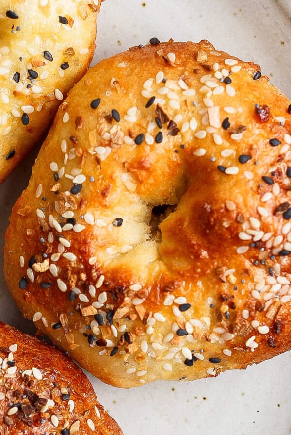 Close-up of three bagels topped with sesame seeds and other seasonings on a beige plate.