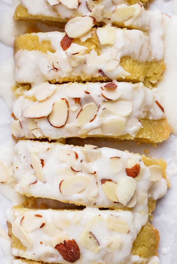 Sliced almond cake topped with white icing and sprinkled with almond slivers.