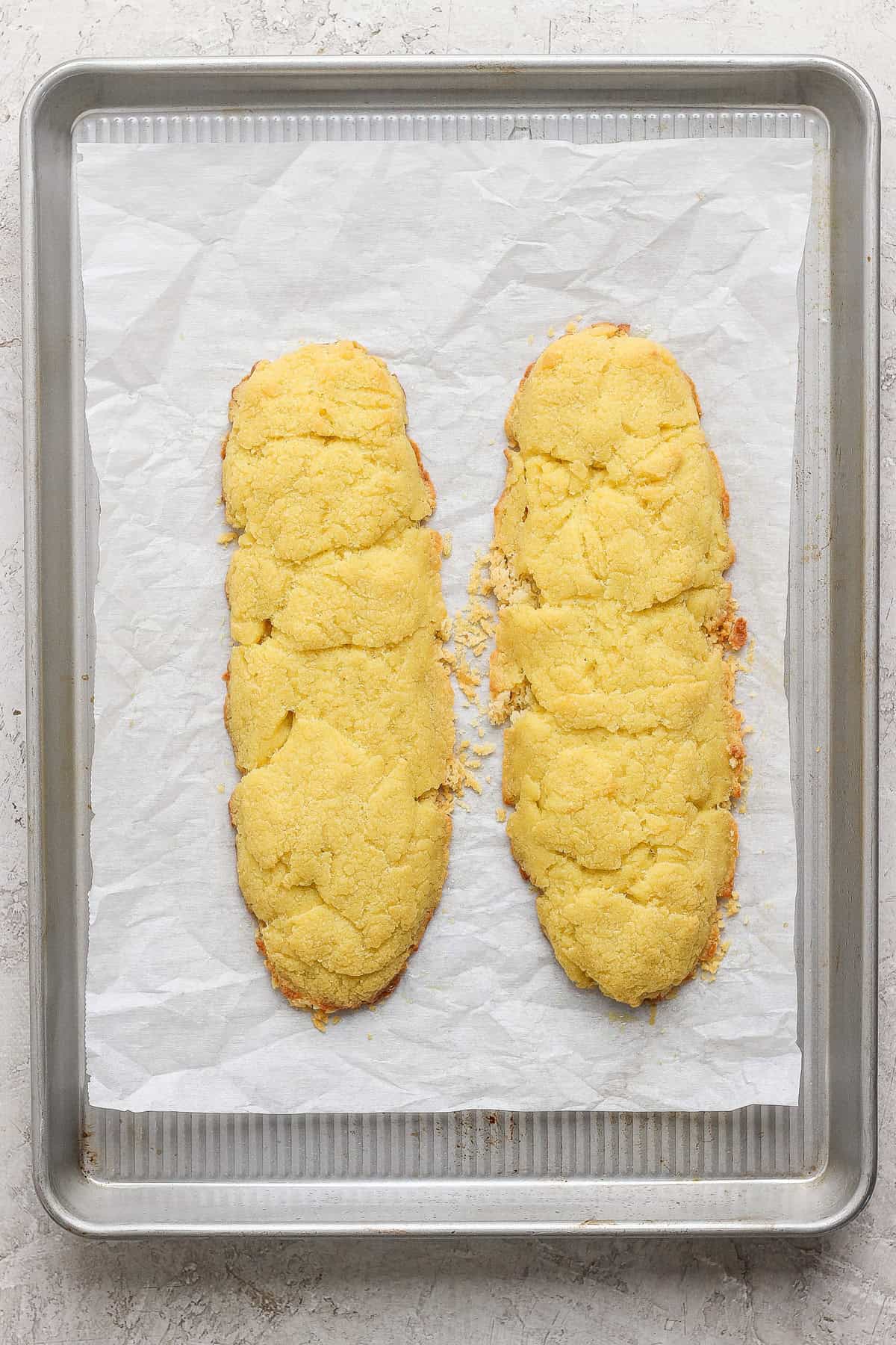 Two homemade almond biscotti cookie logs on a parchment-lined baking sheet.