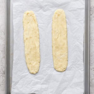 Two unbaked dough logs placed on a parchment-lined baking sheet, ready to be baked.