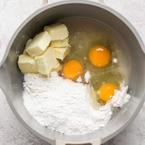 A mixing bowl containing flour, three eggs, and chunks of butter.