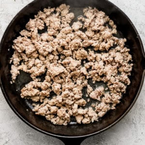 Ground meat cooking in a black cast iron skillet on a light textured surface.