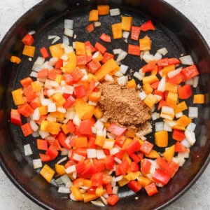 Chopped red, orange, and yellow bell peppers with onions and ground spices in a cast iron skillet.