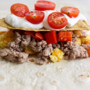 Taco with ground meat, diced red peppers, pineapple, and cherry tomatoes, topped with sour cream.