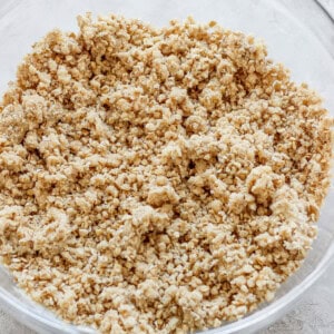 A clear glass bowl filled with a crumbly mixture, likely a streusel or crumble topping, on a light-colored countertop.