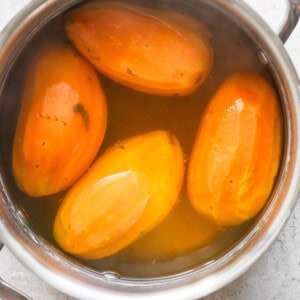 Four peeled sweet potatoes boiling in a stainless steel pot filled with water.